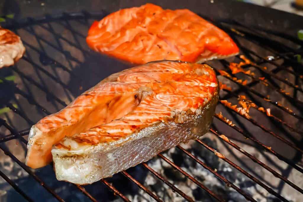 Salmon fillets being grilled on a barbecue, showing grill marks and a slightly charred appearance.