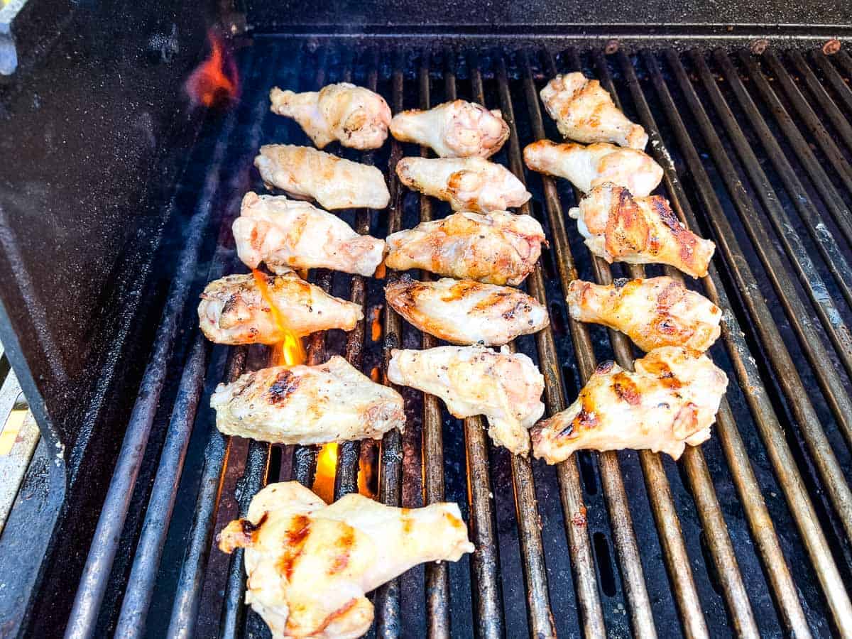 Chicken wings grilling on a barbecue with flames visible below the grates.