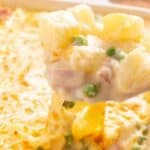 A creamy potato casserole with peas, topped with melted cheese, being served with a wooden spoon.