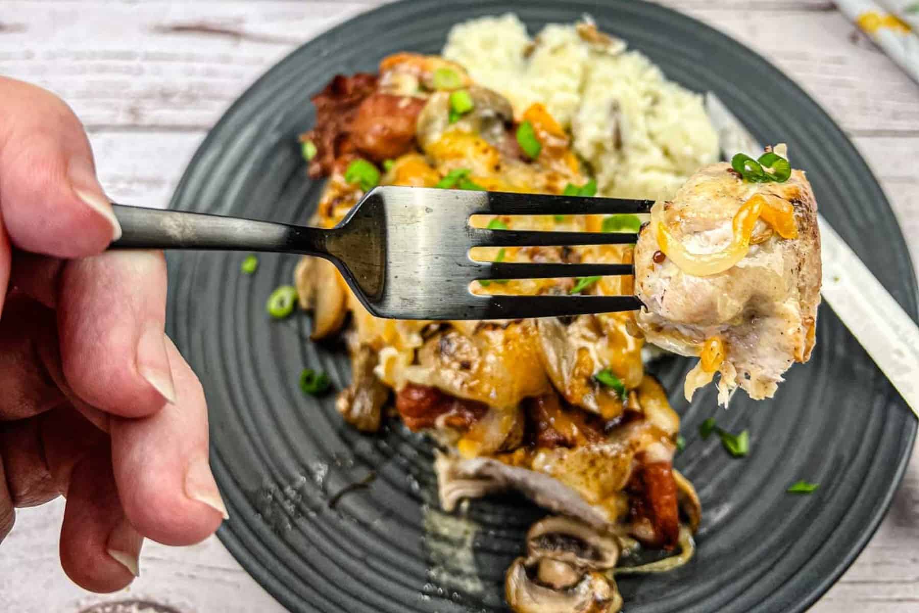 Close-up of a hand holding a fork with a bite of copycat Alice spring chicken.