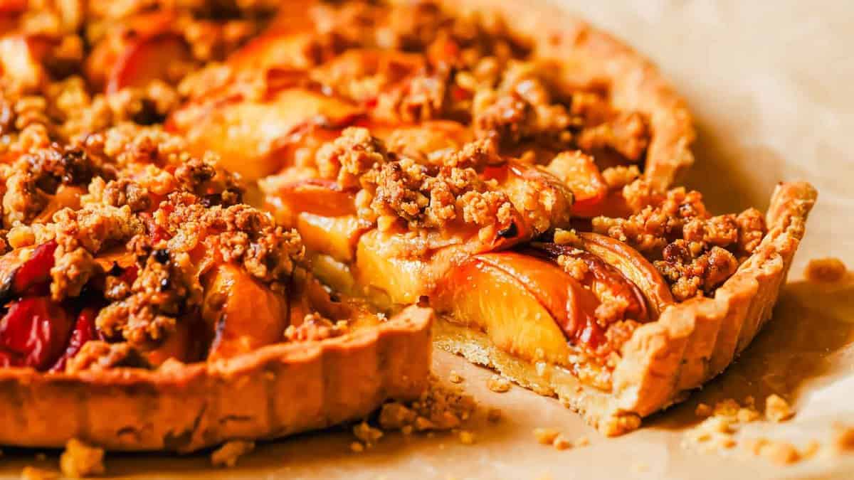 A slice of peach tart with streusel crumble slightly removed from the rest of the tart.