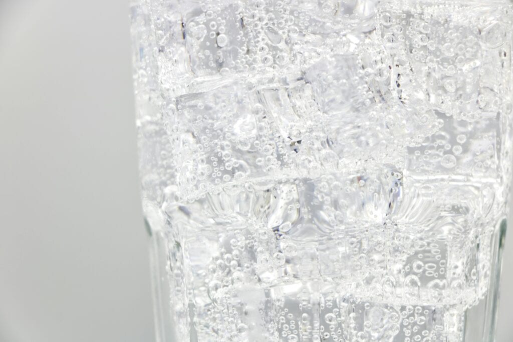 A close-up view of a glass filled with clear, sparkling water and ice cubes.