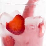 Close-up of a glass containing ice cubes and strawberry slices, with a visible pinkish hue to the liquid.