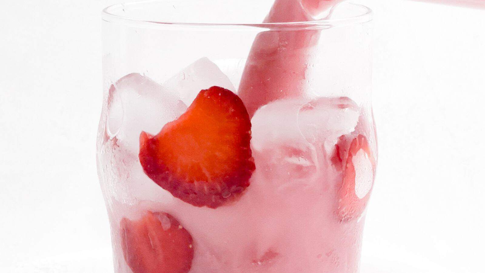 A close-up view of a glass filled with ice and sliced strawberries, with a pink tinted liquid visible.