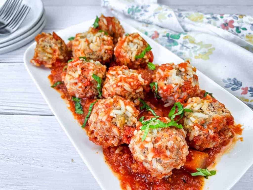 A plate of porcupine meatballs covered in tomato sauce and garnished with fresh basil.