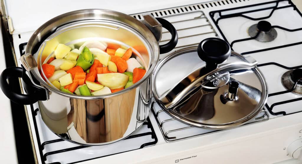 A stainless steel pot with mixed vegetables on a gas stove, next to another pot with a closed lid.