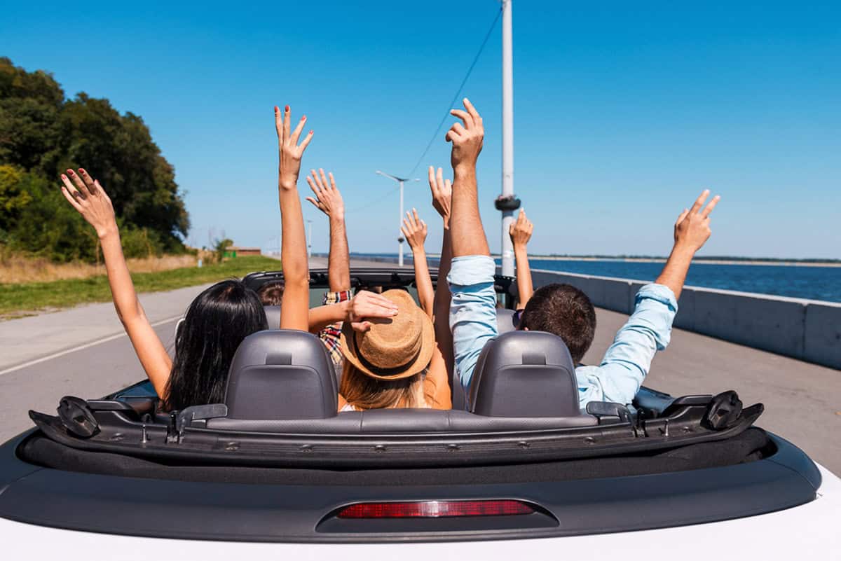 People in a convertible with their hands in the air.