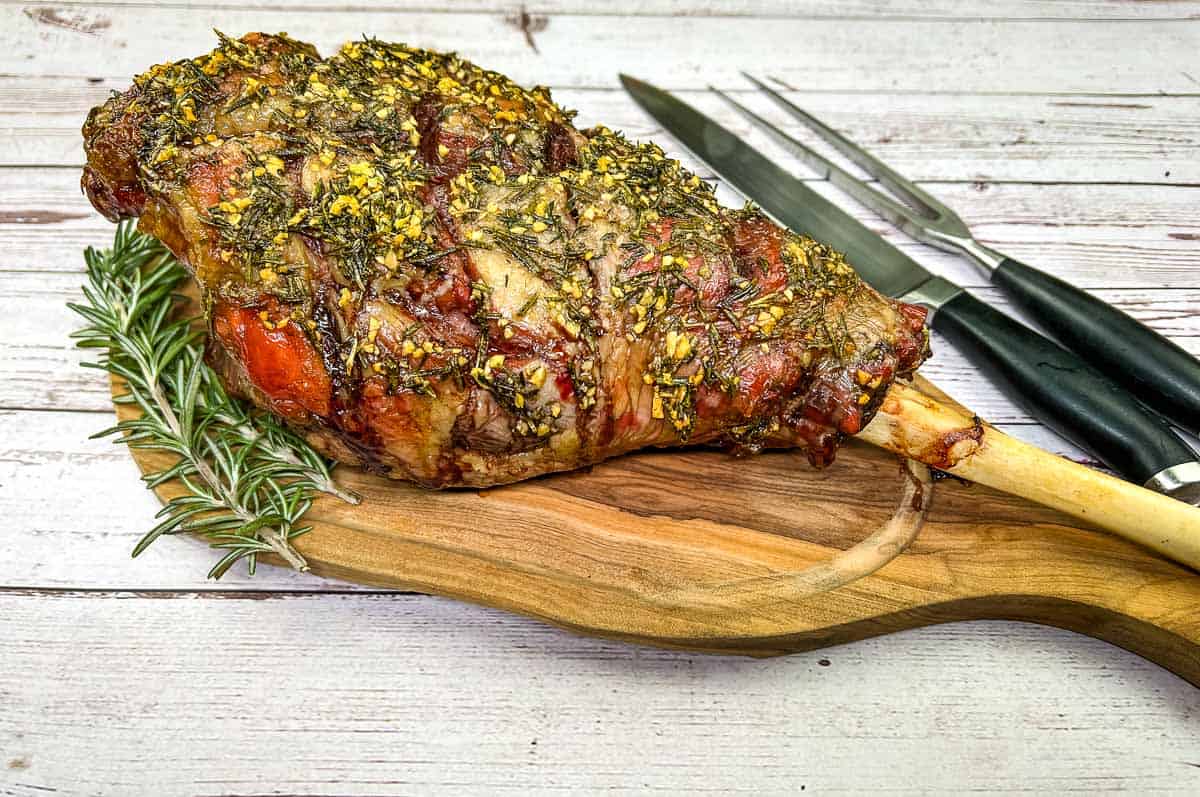 Whole cooked leg of lamb on a board with a knife.