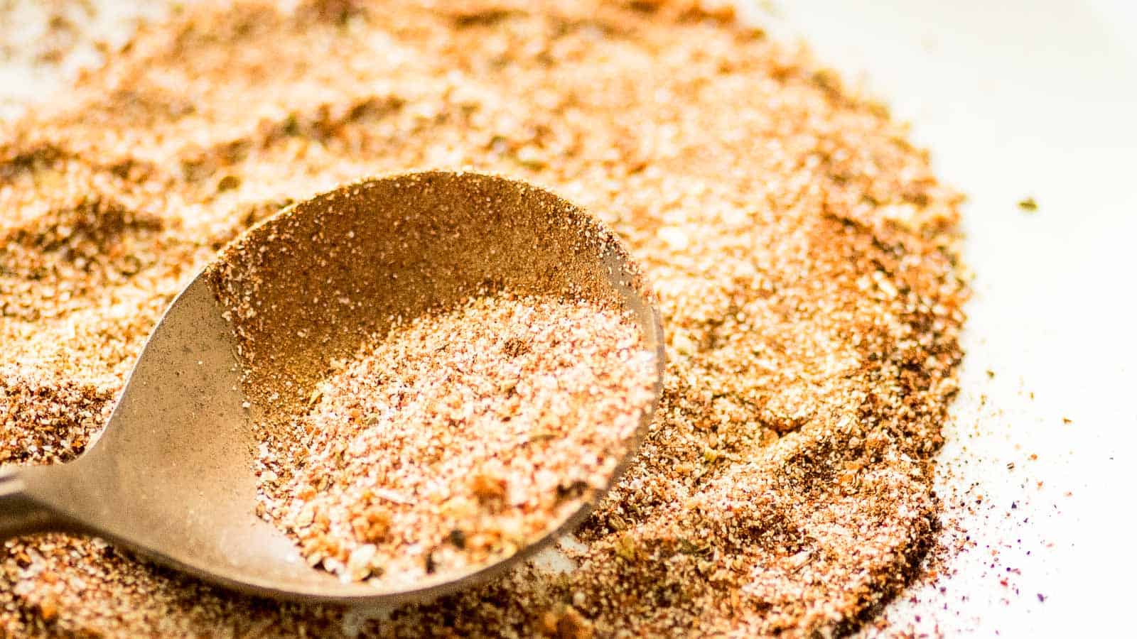 A close-up image of a metal spoon scooping mixed spices and grains on a light surface.