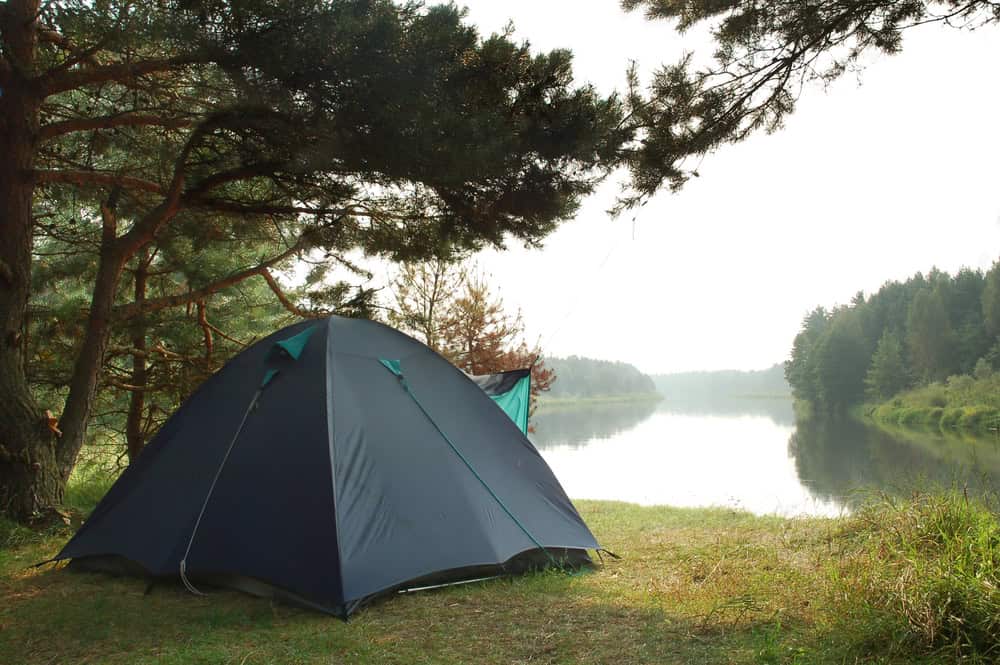 A camping tent in the wilderness in front of a river.