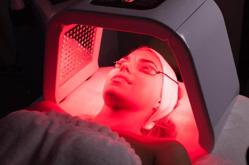 Woman wearing protective eyewear while receiving facial treatment with red light therapy, seeking to understand what is red light therapy.