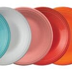 A row of twelve colorful dinner plates arranged in a gradient, ranging from black, purple, blue, turquoise, white, red, orange, to yellow and green.