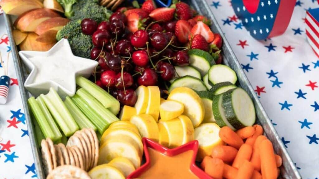 A tray with an assortment of fresh fruits and vegetables and star-shaped dipping bowls.