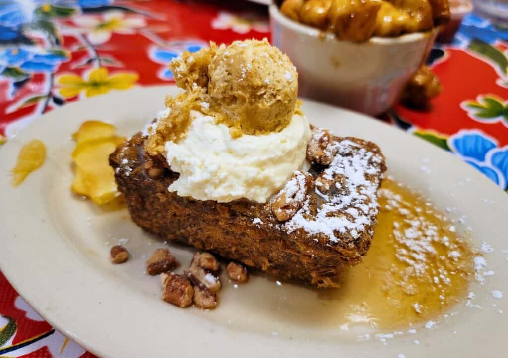 A mini loaf of banana bread topped with whipped cream and pecans on a white plate.