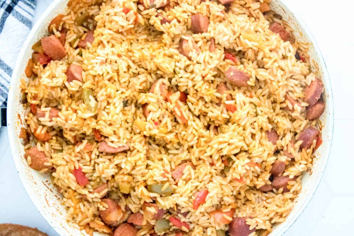 Pan of cajun rice and sausage with a wooden spoon and a bowl.