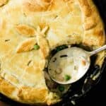 A close-up of a pot pie with a golden-brown crust, partially cut to reveal a creamy filling with peas and chunks of meat. A spoon rests in the filling, indicating it has been served—one of the timeless May recipes enjoyed by many.