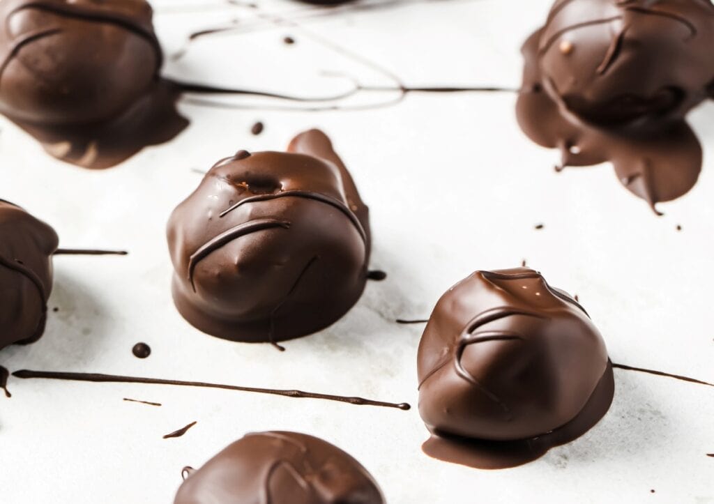 Close-up of several chocolate-dipped truffles on a white surface, with drizzles of melted chocolate scattered around.