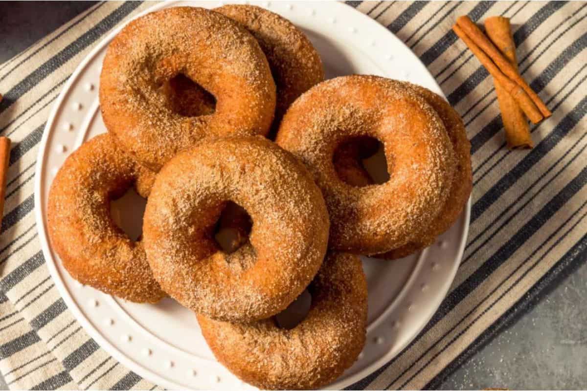 Cinnamon donuts on a plate with cinnamon sticks.