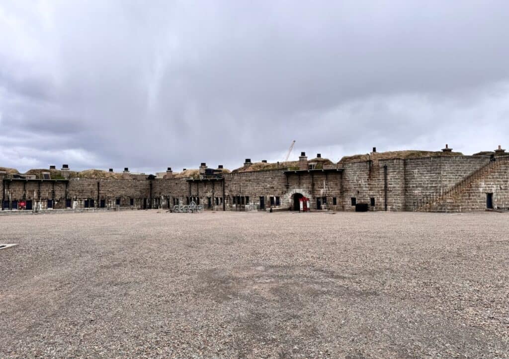 A large stone fort with tall walls, multiple archways, and a spacious gravel courtyard under a cloudy sky.
