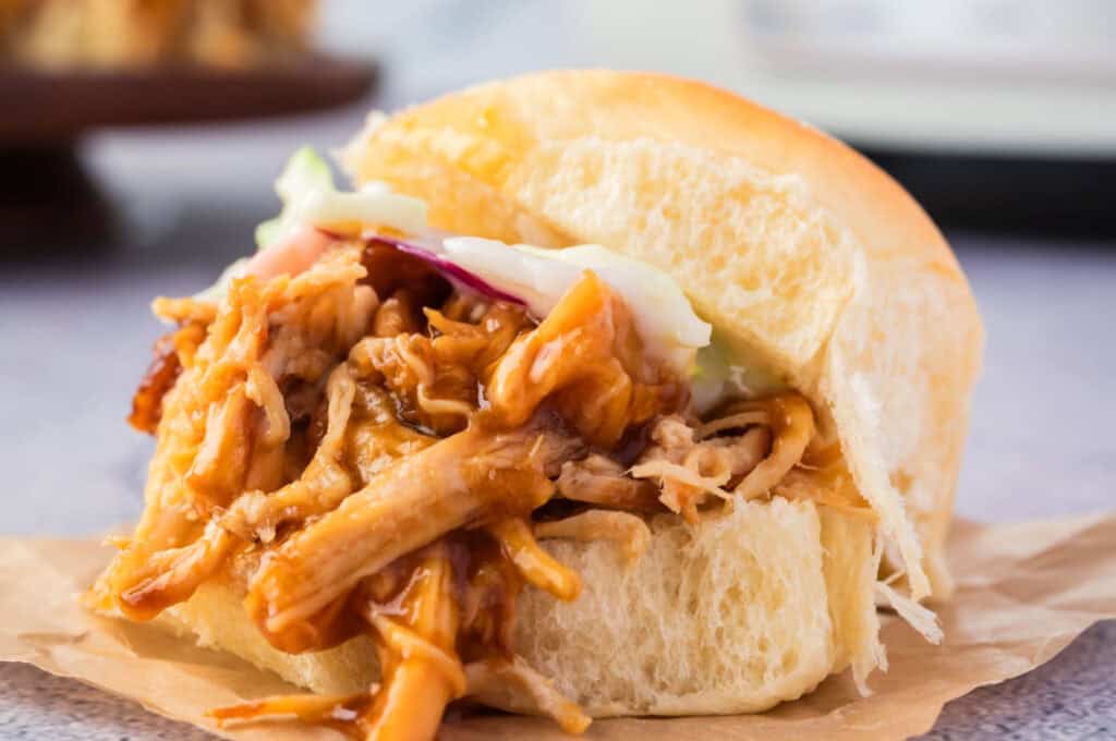 A close-up of a pulled pork slider with coleslaw, served on a soft bun.