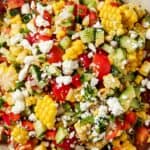 A colorful salad featuring corn, cucumbers, tomatoes, red peppers, and topped with crumbled cheese.