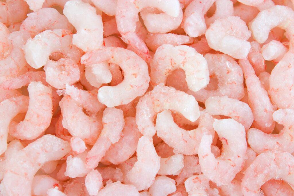 Close-up view of a pile of uncooked, frozen shrimp with a light coating of frost.