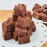 A plate of chocolate fudge squares is stacked into a pyramid, with another plate of fudge squares in the background.