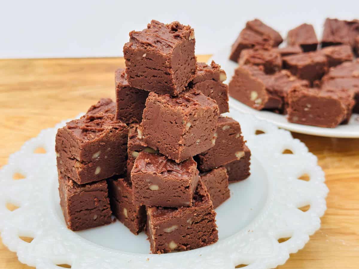 A plate of chocolate fudge squares is stacked into a pyramid, with another plate of fudge squares in the background.