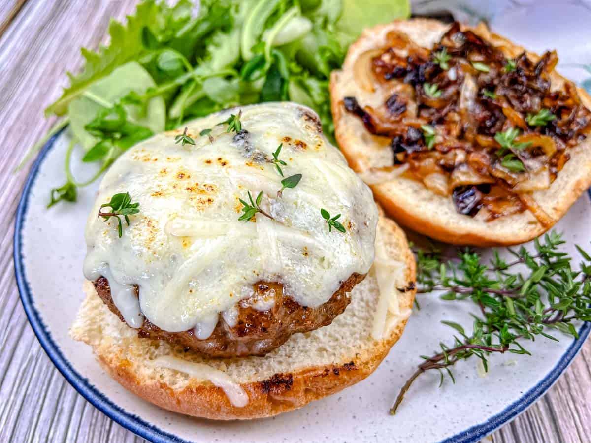 Close-up shot of Grilled French Onion Pork Burgers on a Ninja Woodfire Outdoor Grill topped with cheesy onion on a plate.