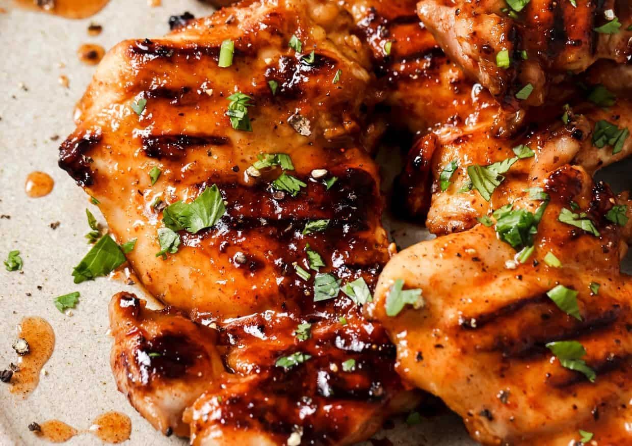 Grilled chicken pieces with a glossy glaze, garnished with chopped herbs, served on a beige plate.