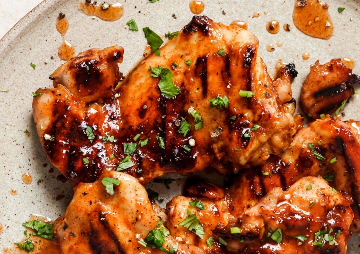 Grilled chicken pieces with a glossy glaze, garnished with chopped herbs, served on a beige plate.