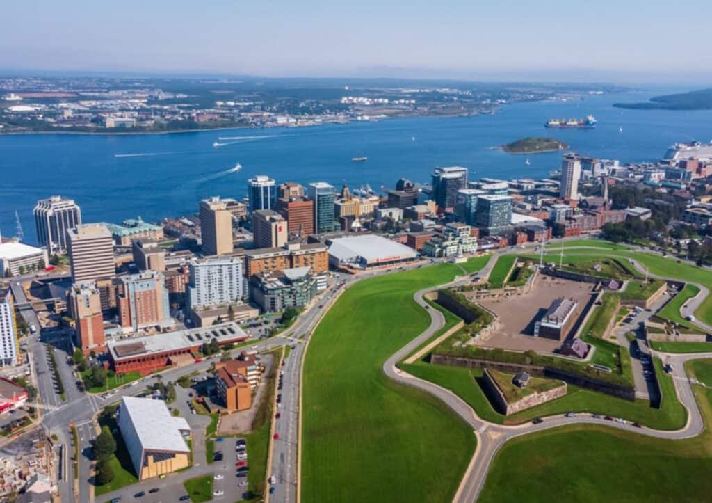 Aerial view of a coastal city featuring a waterfront, modern buildings, and a historical fort surrounded by green spaces—discover the top things to do in Halifax.