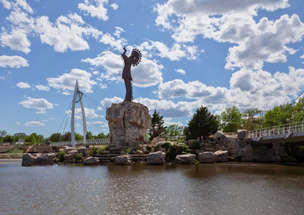 A tall Native American statue stands on a rock above two merging rivers.