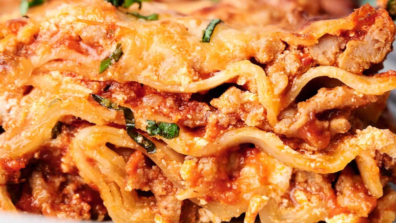 Close-up of a delicious slice of lasagna, showcasing layers of pasta, ground meat, tomato sauce, ricotta cheese, and garnished with chopped basil.