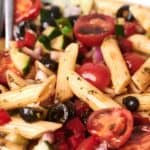A bowl of pasta salad with penne, cherry tomatoes, black olives, cucumbers, red onions, bell peppers, and herbs.