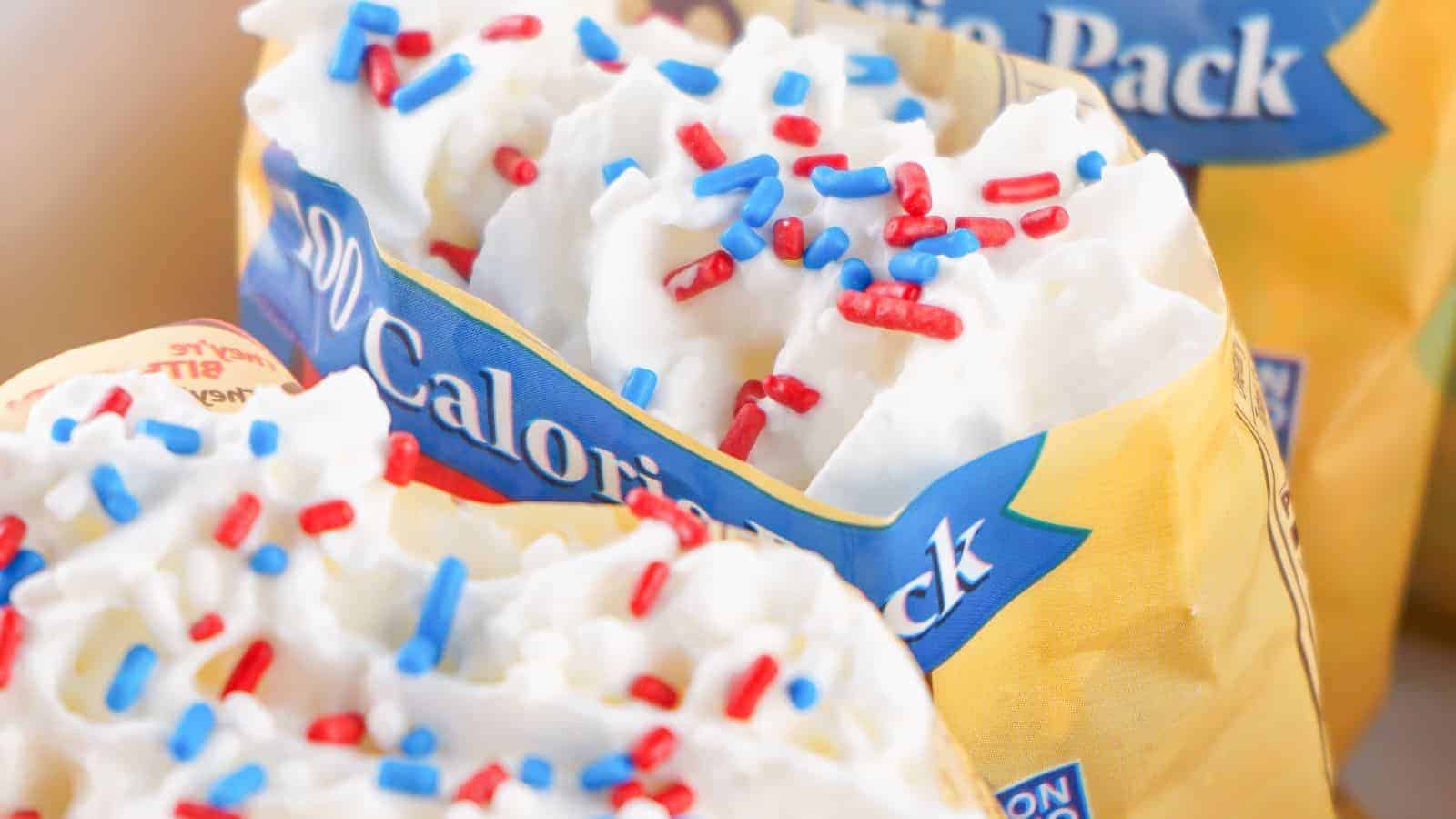 Close-up image of a snack pack filled with whipped cream topped with red, white, and blue sugar sprinkles. Packaging displays 