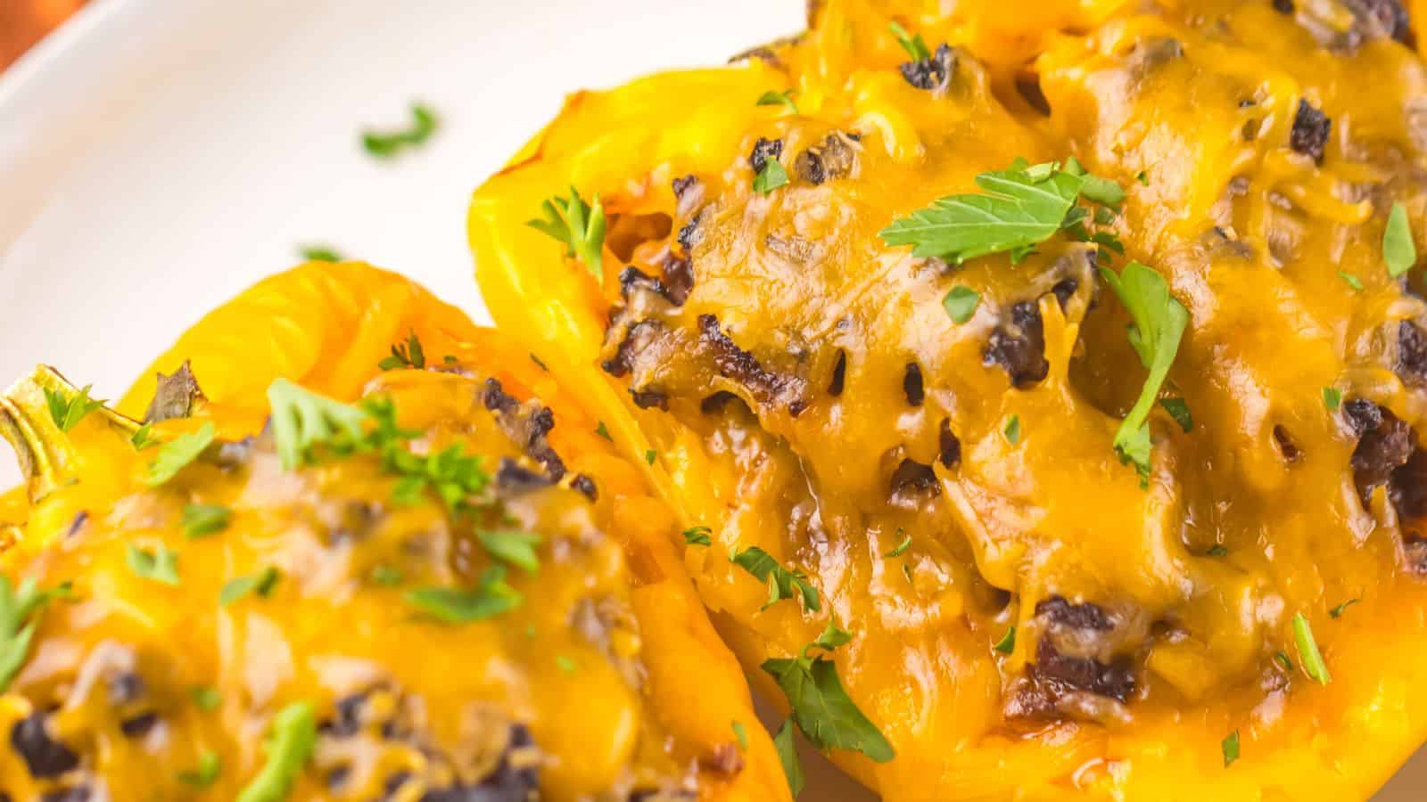 Close-up of two yellow bell peppers stuffed with a mixture of sloppy joe, black beans, and rice, topped with melted cheddar cheese and garnished with chopped parsley.