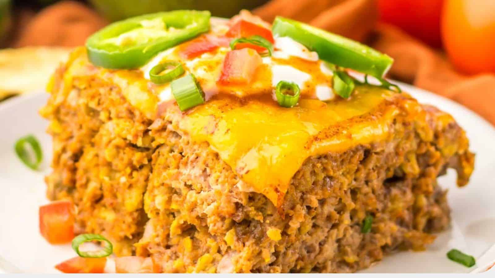 Close-up of a slice of cheesy taco casserole topped with chopped tomatoes, green onions, and jalapeño slices on a white plate, reminiscent of the comforting flavors found in slow cooker taco meatloaf.