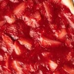 Close-up of a strawberry pie featuring whole and sliced strawberries in a vibrant red filling on a flaky crust.