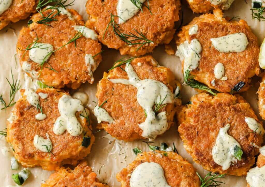 Golden-brown salmon patties topped with dollops of creamy dill sauce and garnished with fresh dill.