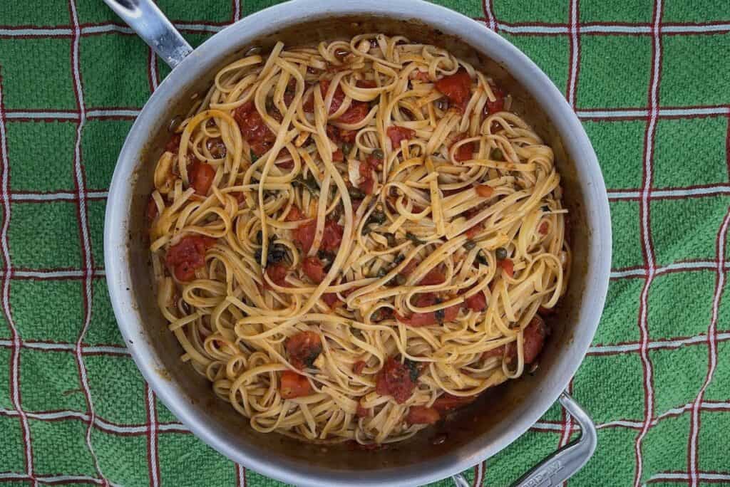 A pan of linguine pasta mixed with tomato sauce and herbs sits on a green and red checkered cloth.