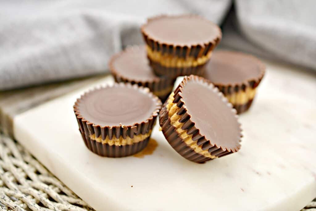 Chocolate peanut butter cups stacked and arranged on a marble cutting board with a cloth in the background.