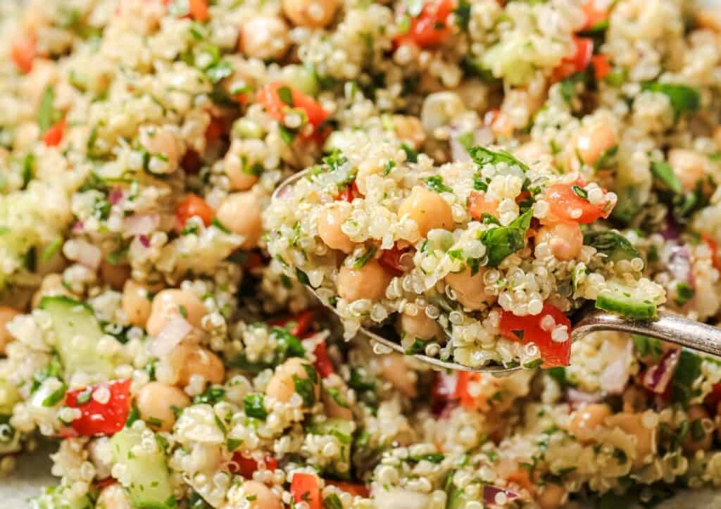 A spoonful of quinoa salad containing quinoa, chickpeas, chopped vegetables, and herbs.