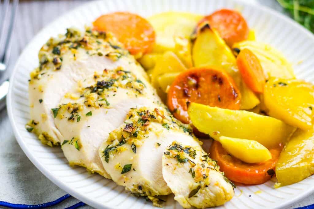 A plate of herb-roasted chicken breast slices served with roasted potatoes and carrots, perfect for your favorite dinner recipes.