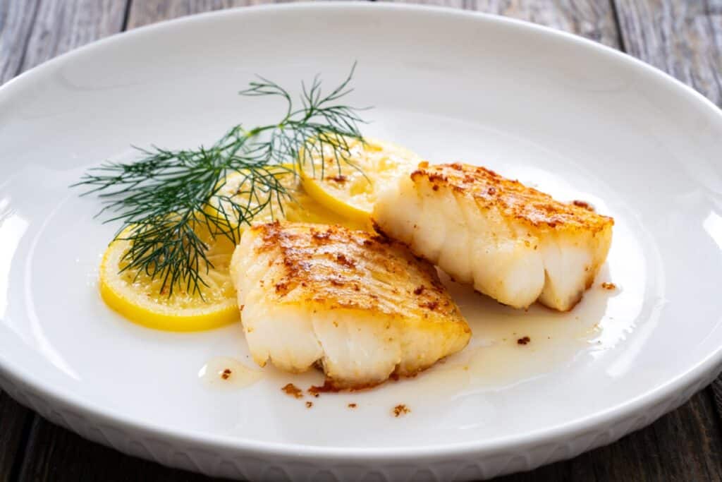 Two grilled fish fillets garnished with lemon slices and dill on a white plate.