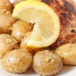A plate with roasted chicken, seasoned baby potatoes, and a lemon wedge.