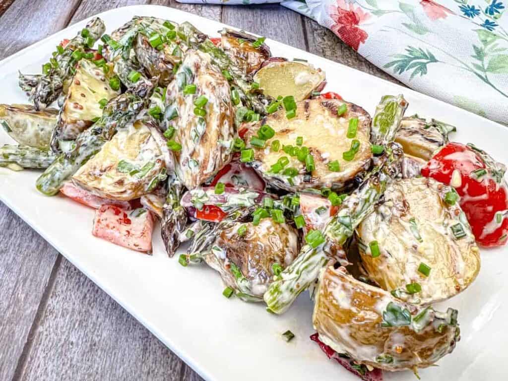 A plate of roasted potato and asparagus salad topped with chopped chives and a creamy dressing.