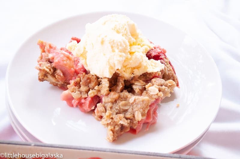 A plate of strawberry rhubarb crisp topped with a scoop of vanilla ice cream.