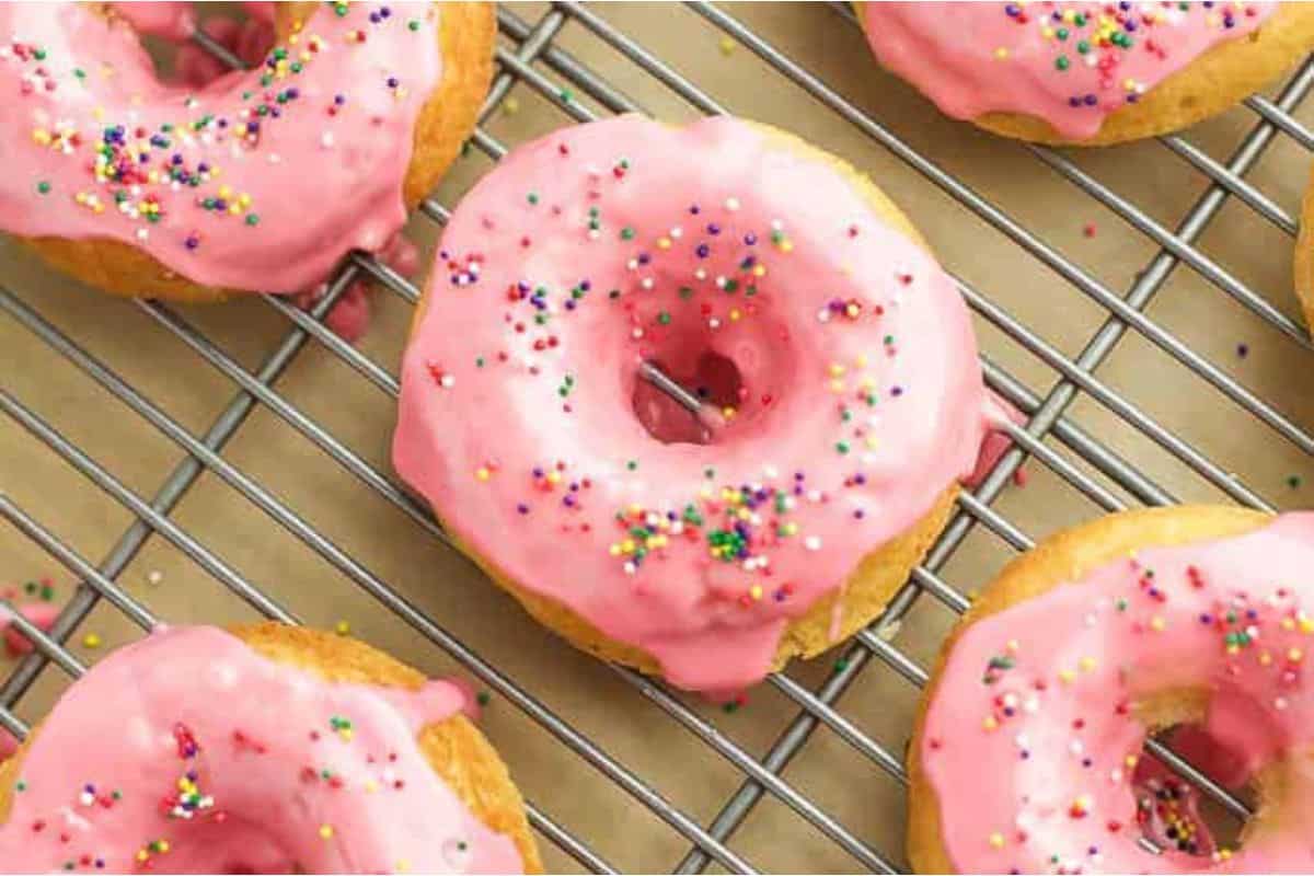 Pink glazed donuts with sprinkles on a cooling rack.