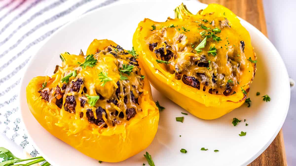 Two stuffed yellow bell peppers with melted cheese and herbs served on a white plate.